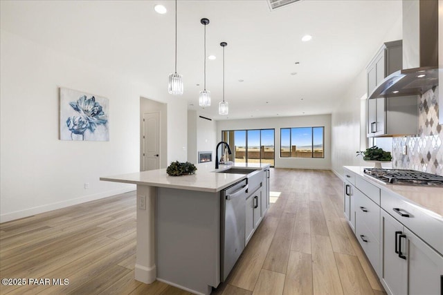 kitchen with wall chimney range hood, a sink, appliances with stainless steel finishes, and light wood-style floors