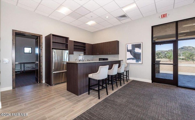 kitchen with a breakfast bar area, a peninsula, visible vents, freestanding refrigerator, and open shelves