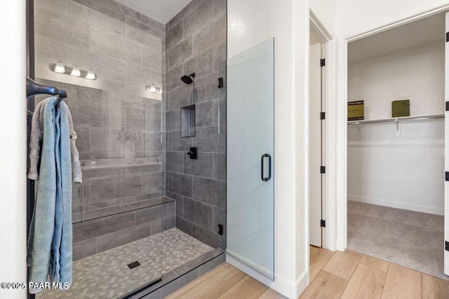 bathroom with a stall shower, a spacious closet, baseboards, and wood finished floors