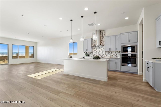 kitchen with visible vents, decorative backsplash, light wood-style floors, stainless steel appliances, and wall chimney range hood