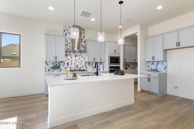 kitchen with light countertops, visible vents, light wood-style flooring, appliances with stainless steel finishes, and wall chimney range hood