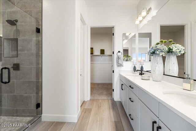 full bath featuring a stall shower, double vanity, a sink, and wood finished floors