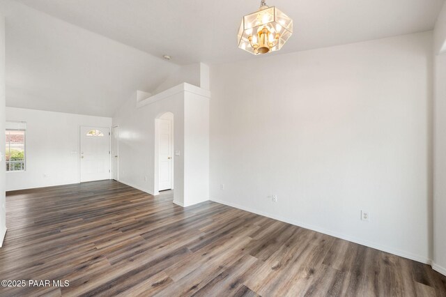 unfurnished room with lofted ceiling, arched walkways, an inviting chandelier, and dark wood finished floors