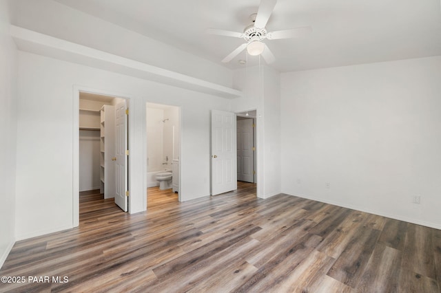 unfurnished bedroom with wood finished floors, baseboards, a closet, ensuite bathroom, and a walk in closet