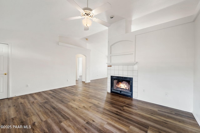 unfurnished living room featuring arched walkways, a fireplace, lofted ceiling, and wood finished floors