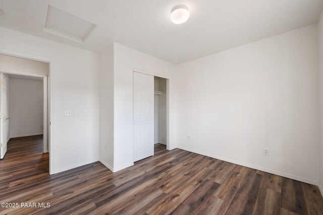 unfurnished bedroom featuring dark wood finished floors, attic access, baseboards, and a closet