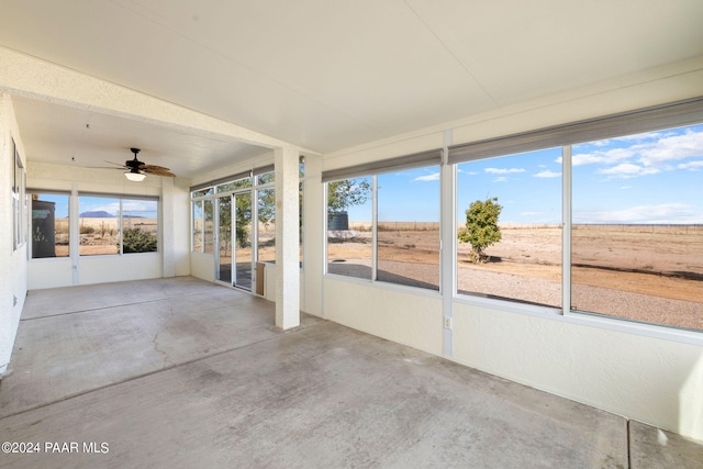 unfurnished sunroom with ceiling fan and a rural view