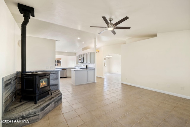 living room featuring vaulted ceiling, ceiling fan, sink, light tile patterned floors, and a wood stove