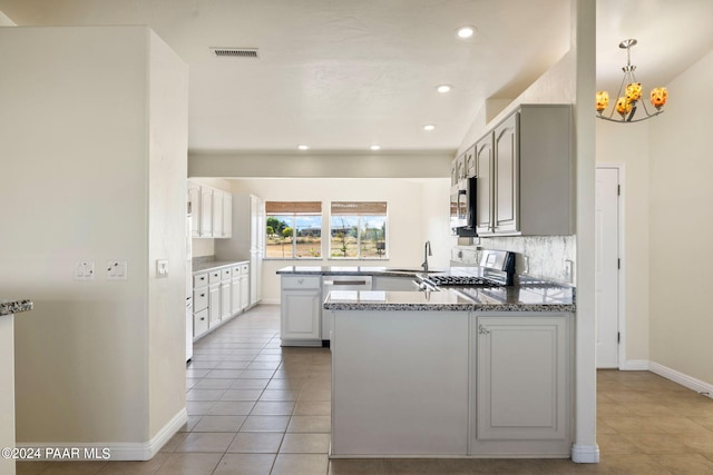 kitchen featuring a notable chandelier, backsplash, kitchen peninsula, light tile patterned flooring, and appliances with stainless steel finishes