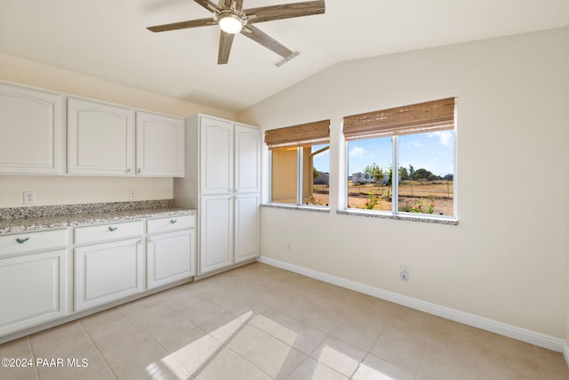 kitchen with baseboards, lofted ceiling, ceiling fan, light stone counters, and white cabinetry