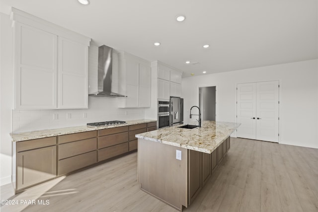 kitchen with sink, white cabinets, light hardwood / wood-style floors, and wall chimney range hood