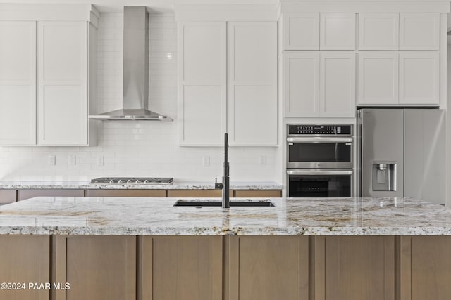 kitchen featuring light stone countertops, sink, wall chimney exhaust hood, stainless steel appliances, and white cabinets