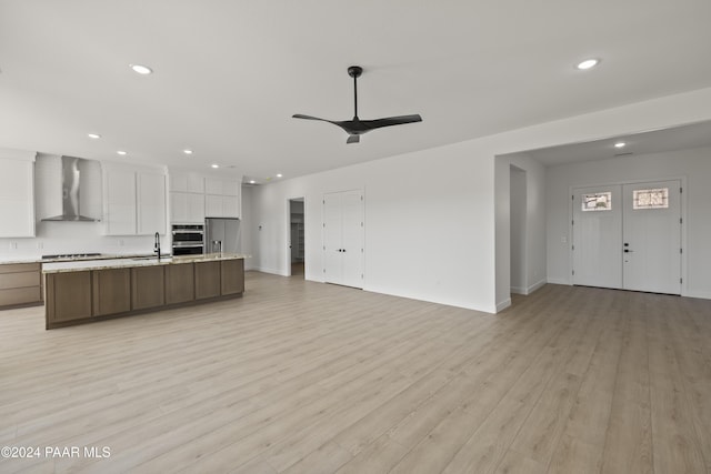 kitchen with white cabinets, wall chimney exhaust hood, sink, and light hardwood / wood-style flooring