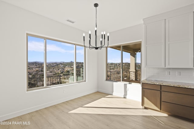 unfurnished dining area with a wealth of natural light, an inviting chandelier, and light wood-type flooring