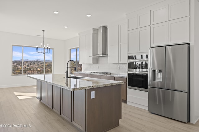 kitchen with light stone countertops, white cabinetry, wall chimney exhaust hood, hanging light fixtures, and stainless steel appliances