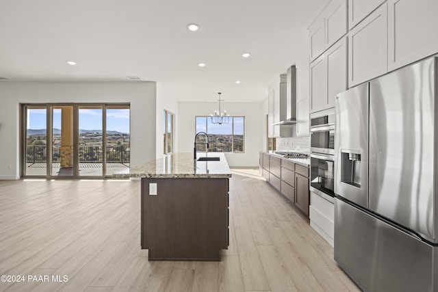 kitchen featuring appliances with stainless steel finishes, wall chimney range hood, pendant lighting, a mountain view, and an island with sink