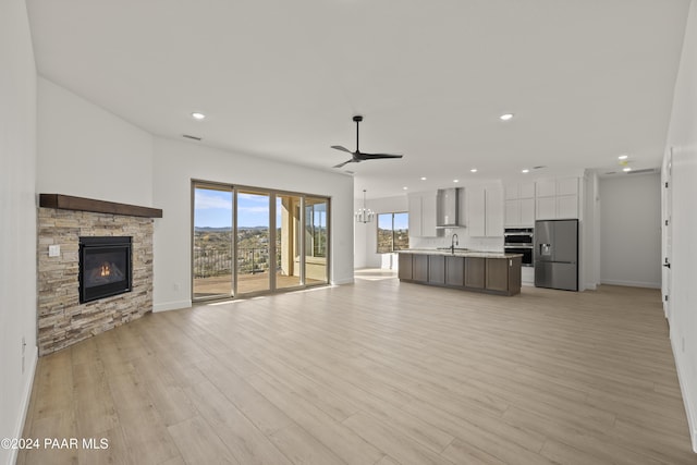 unfurnished living room featuring ceiling fan, a fireplace, sink, and light wood-type flooring