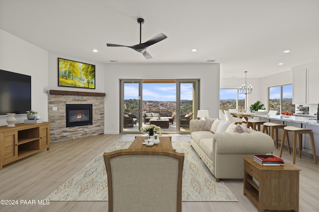 living room with ceiling fan with notable chandelier, light hardwood / wood-style floors, a fireplace, and a wealth of natural light