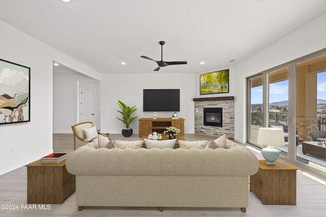 living room with a stone fireplace, ceiling fan, and light wood-type flooring