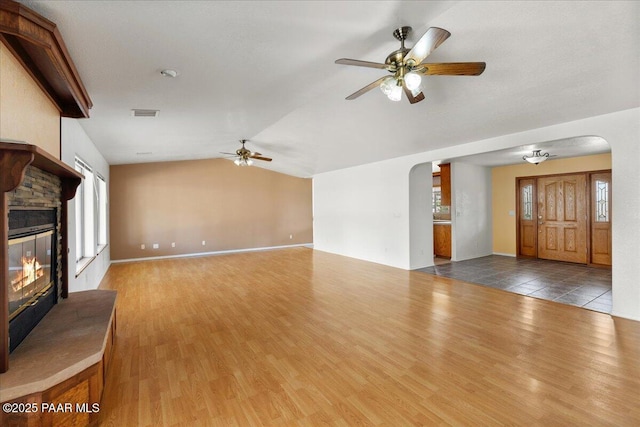 20775 N Hackamore Ln, Paulden, AZ 86334 - unfurnished living room featuring arched walkways, ceiling fan, lofted ceiling, a stone fireplace, and healthy amount of natural light