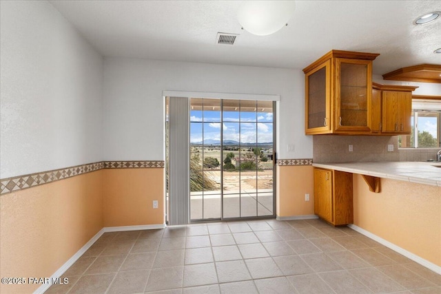 20775 N Hackamore Ln, Paulden, AZ 86334 - kitchen featuring brown cabinetry, glass insert cabinets, tile countertops, baseboards, and light tile patterned flooring