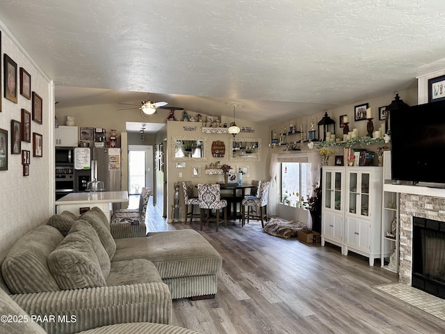 living room with a stone fireplace, lofted ceiling, hardwood / wood-style flooring, ceiling fan, and a textured ceiling