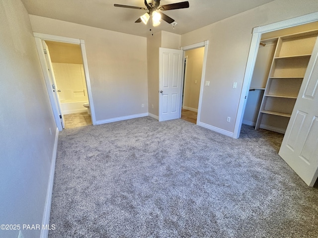 unfurnished bedroom with a spacious closet, baseboards, carpet flooring, ensuite bathroom, and a ceiling fan