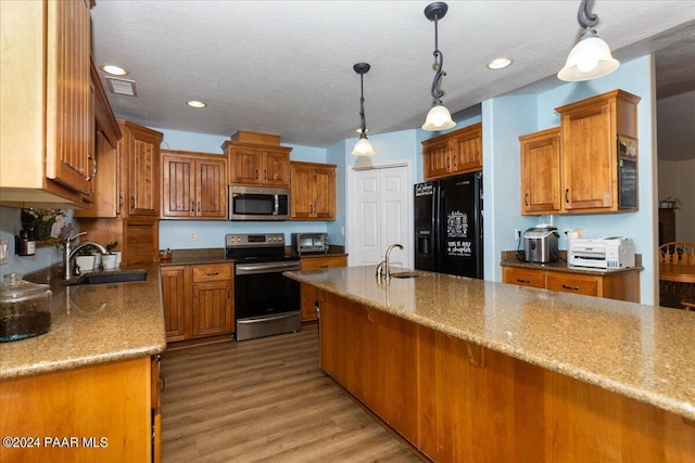 kitchen featuring sink, light hardwood / wood-style floors, pendant lighting, a textured ceiling, and appliances with stainless steel finishes