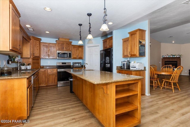 kitchen with a center island with sink, stainless steel appliances, decorative light fixtures, and light wood-type flooring