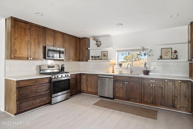 kitchen featuring tasteful backsplash, stainless steel appliances, sink, and light hardwood / wood-style flooring