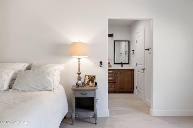 bedroom with connected bathroom, sink, and light wood-type flooring