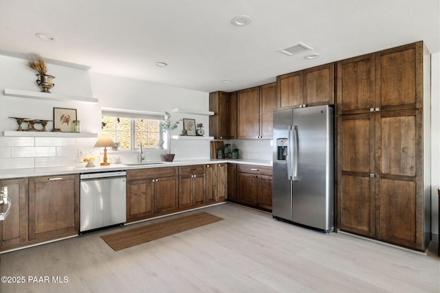 kitchen with stainless steel appliances, tasteful backsplash, sink, and light hardwood / wood-style floors