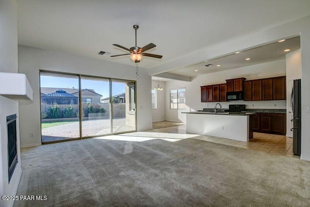 kitchen featuring sink, an island with sink, light colored carpet, black appliances, and ceiling fan with notable chandelier