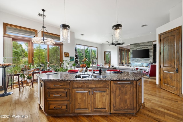 kitchen with a kitchen island with sink, sink, ceiling fan, and dark stone counters