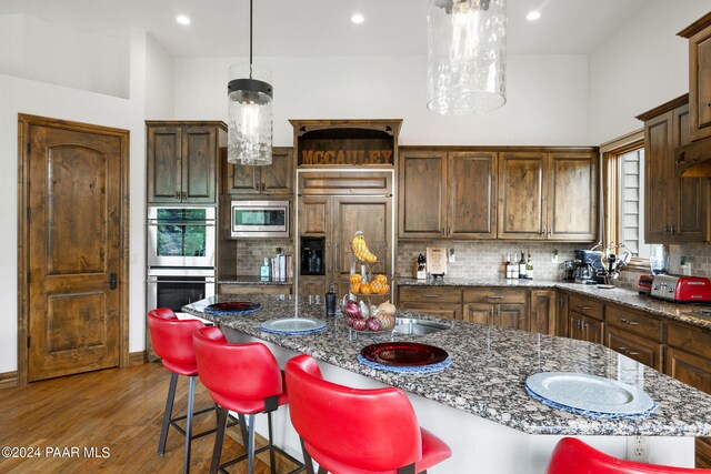 kitchen with a center island with sink, dark stone countertops, built in appliances, and hanging light fixtures