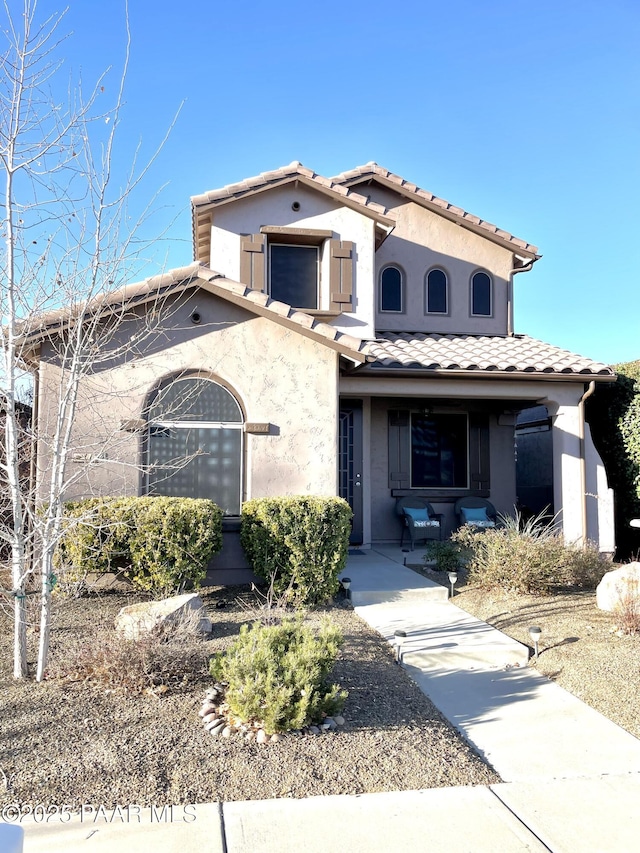 mediterranean / spanish house featuring a porch, stucco siding, and a tiled roof