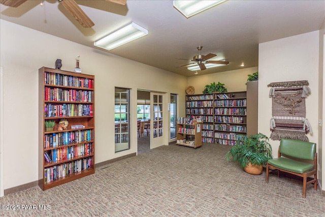 sitting room featuring french doors, bookshelves, a ceiling fan, carpet flooring, and baseboards
