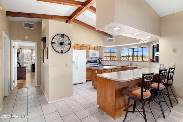 kitchen with a peninsula, white appliances, visible vents, brown cabinetry, and a kitchen bar