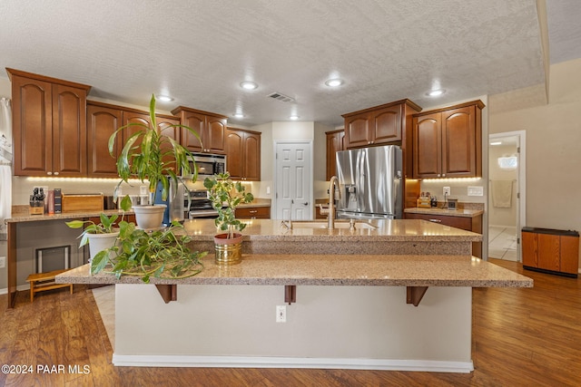 kitchen with a center island with sink, a kitchen breakfast bar, stainless steel appliances, and dark wood-type flooring