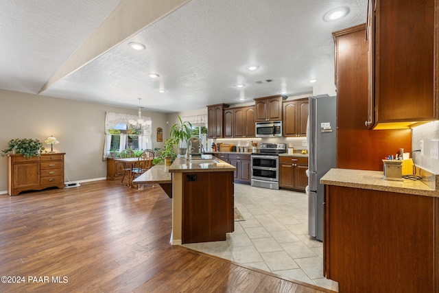 kitchen featuring a breakfast bar, sink, light hardwood / wood-style flooring, an island with sink, and appliances with stainless steel finishes