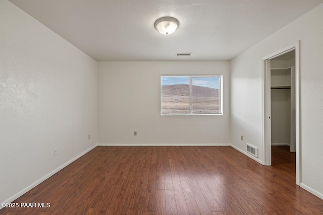 unfurnished bedroom with visible vents, baseboards, wood finished floors, and a spacious closet