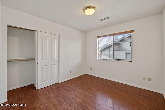 unfurnished bedroom featuring a closet, visible vents, baseboards, and wood finished floors