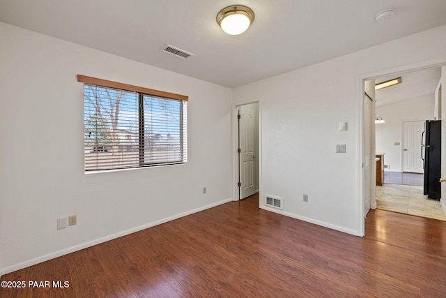 unfurnished bedroom with visible vents, wood finished floors, and freestanding refrigerator