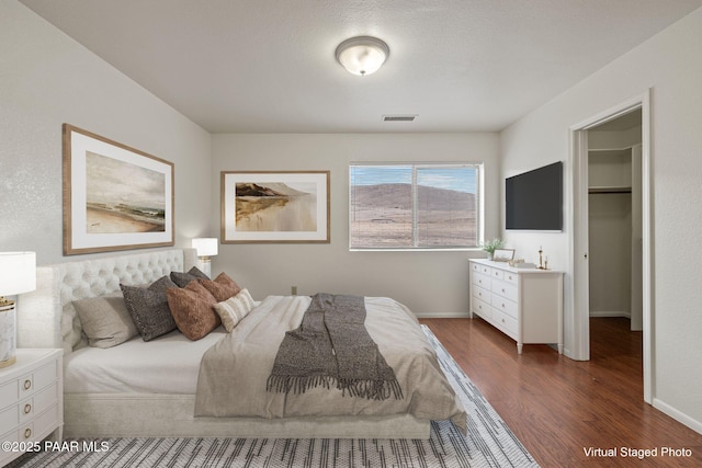 bedroom featuring a spacious closet, wood finished floors, visible vents, and baseboards