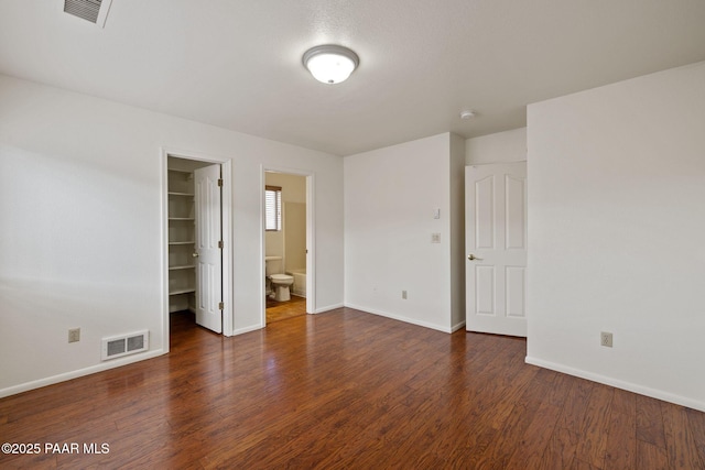 unfurnished bedroom with a spacious closet, visible vents, and wood finished floors