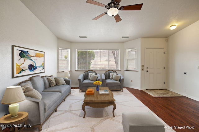 living area with a ceiling fan, baseboards, wood finished floors, visible vents, and a textured ceiling