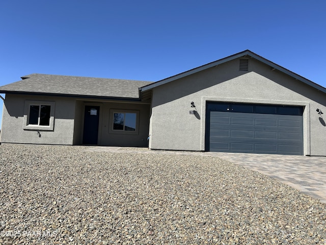 ranch-style home featuring stucco siding, an attached garage, decorative driveway, and roof with shingles