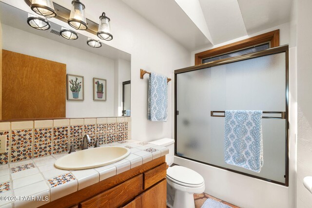 bathroom with toilet, vanity, enclosed tub / shower combo, and decorative backsplash