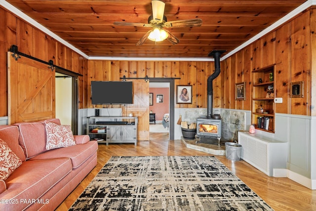 living room featuring wooden walls, wood ceiling, a wood stove, and a barn door