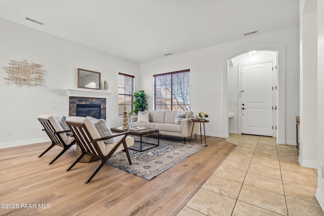 living area with visible vents, a stone fireplace, light wood-type flooring, and arched walkways